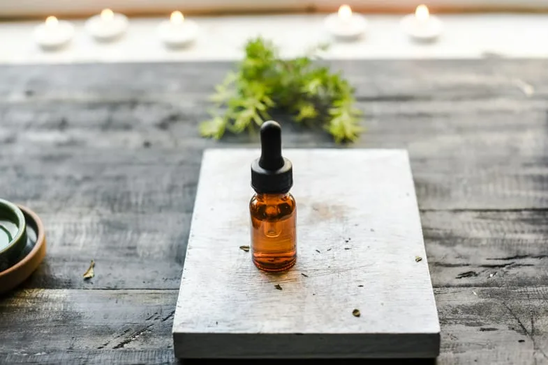 bottle of CBD oil above a small table with marijuana leaves in the background | Justbob