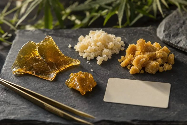 Amber shatter, pale CBD crystals, matte crumble and wax-like extract samples on dark slate