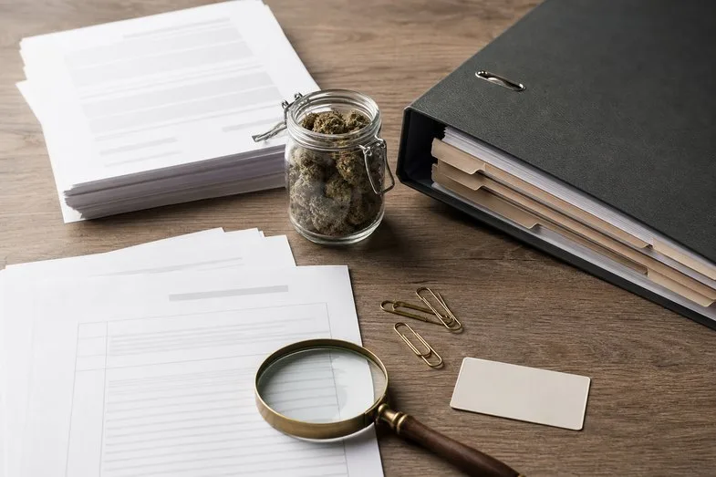 CBD legal in Europe document scene with hemp flower jar, binder, blank certificate sheets and magnifier