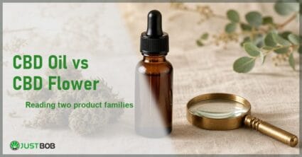 Justbob CBD Oil Vs CBD Flower banner with green title, an amber oil bottle, hemp flower buds and a brass loupe on cream linen