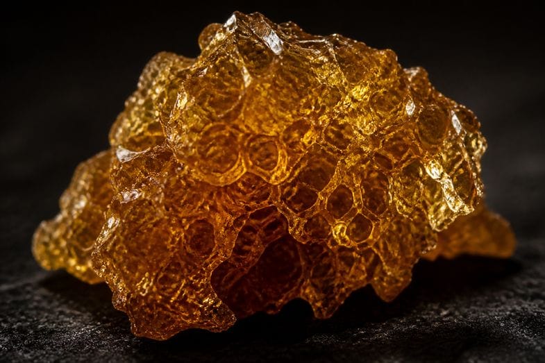 cbd-crumble-documents Extreme macro of amber CBD crumble extract with a glistening crystalline honeycomb texture on a dark surface