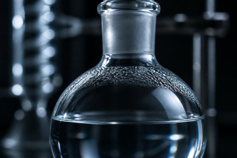 hhc-vs-thc-glassware-macro Macro of a round-bottomed glass flask holding clear liquid, with fine condensation beads across its shoulder