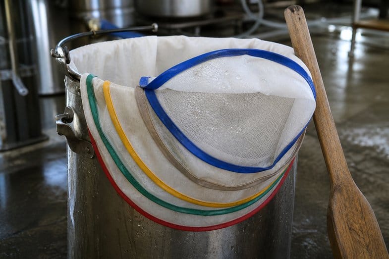 triple-filtered-hash-mesh-bags Nested filtration bags with blue, green, yellow and red rims hanging over a stainless bucket, one folded back