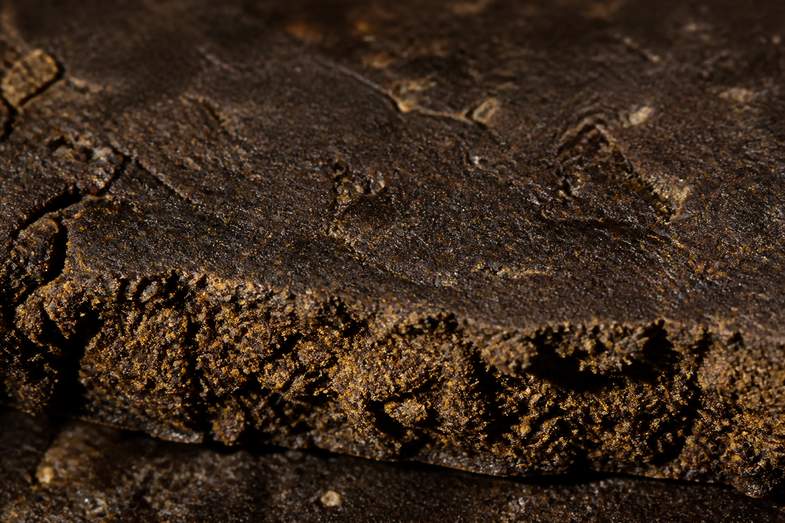 triple-filtered-hash-pressed-slab Extreme macro of the matte surface of a dark brown pressed resin slab, granular and marked by compression